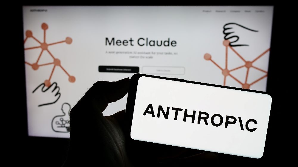 Person holding mobile phone with logo of US artificial intelligence company Anthropic and in the background Meet Claude is on a laptop screen, in story about Anthropic's deal with Amazon.
