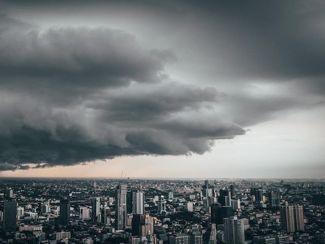 visible storm blowing over a city, half the city in shadows, the other half still in sunlight