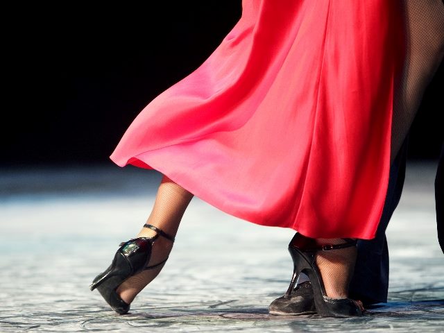A woman in a flowing and silky dark pink dress and black high heels dances with a man wearing dress shoes suggesting the dance between AI and empathy in customer experience.