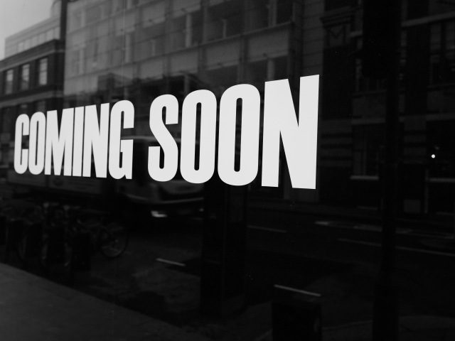 A coming soon sign on the side of the building. The total image is in black and white.