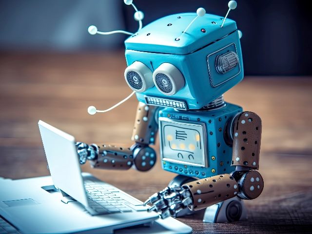 A blue robot types on a laptop computer in an office suggesting the use of AI in customer experience in call centers. 