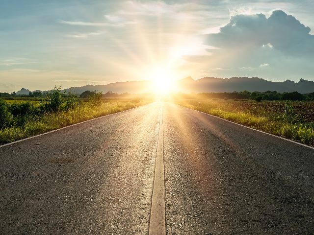 An asphalt road heading. into a brilliant sunset in a rural setting with hills and clouds in the background in piece about AI in customer journey mapping.
