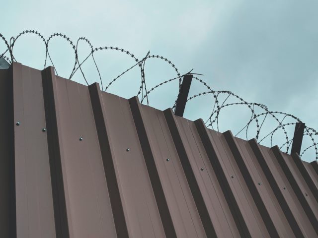 brown steel fence with barbed wire at the top