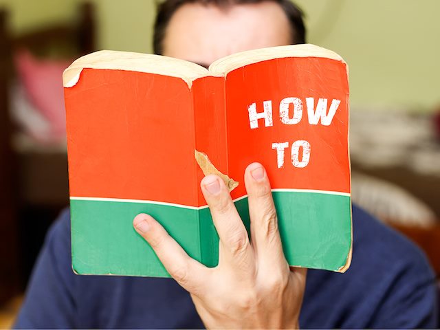 Person holding an open book with title How To in front of their face