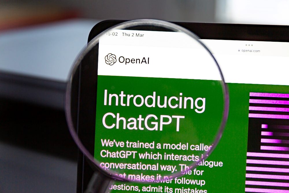 The OpenAI page introducing ChatGPT is visible through a magnifying glass in piece about growing use of AI in customer experience.