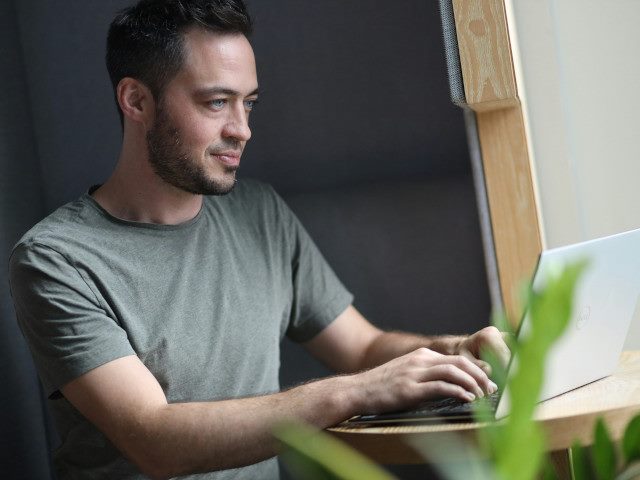 An employee works on a laptop computer in an office enclosure.