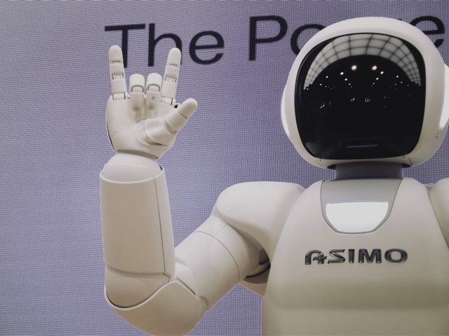 A white robot with a black glossy faceplate raising one hand in the rock-and-roll "hand horns" gesture.