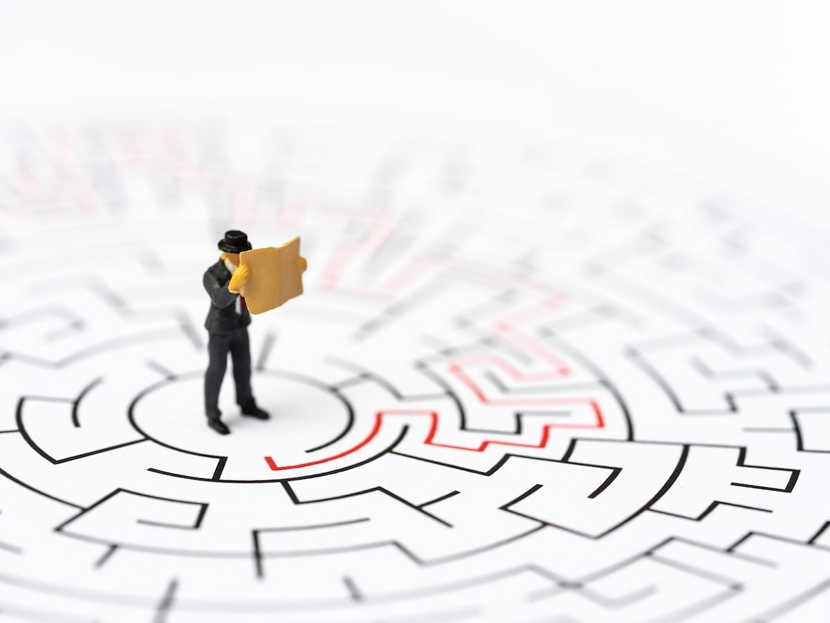 A businessman figuring holding a map and standing in the middle of a maze