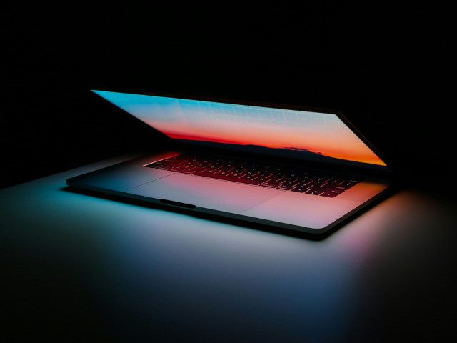 A half-open Apple MacBook laptop in the dark.