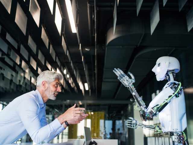 Mature businessman or a scientist with gray hair with a robot/artificial intelligence (AI)