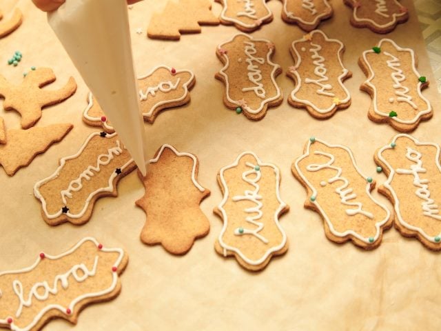 Decorating cookies with icing tube, writing names and ornaments on homemade cookies. 
