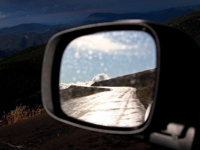 side-view mirror showing a road and a mountainous backdrop.