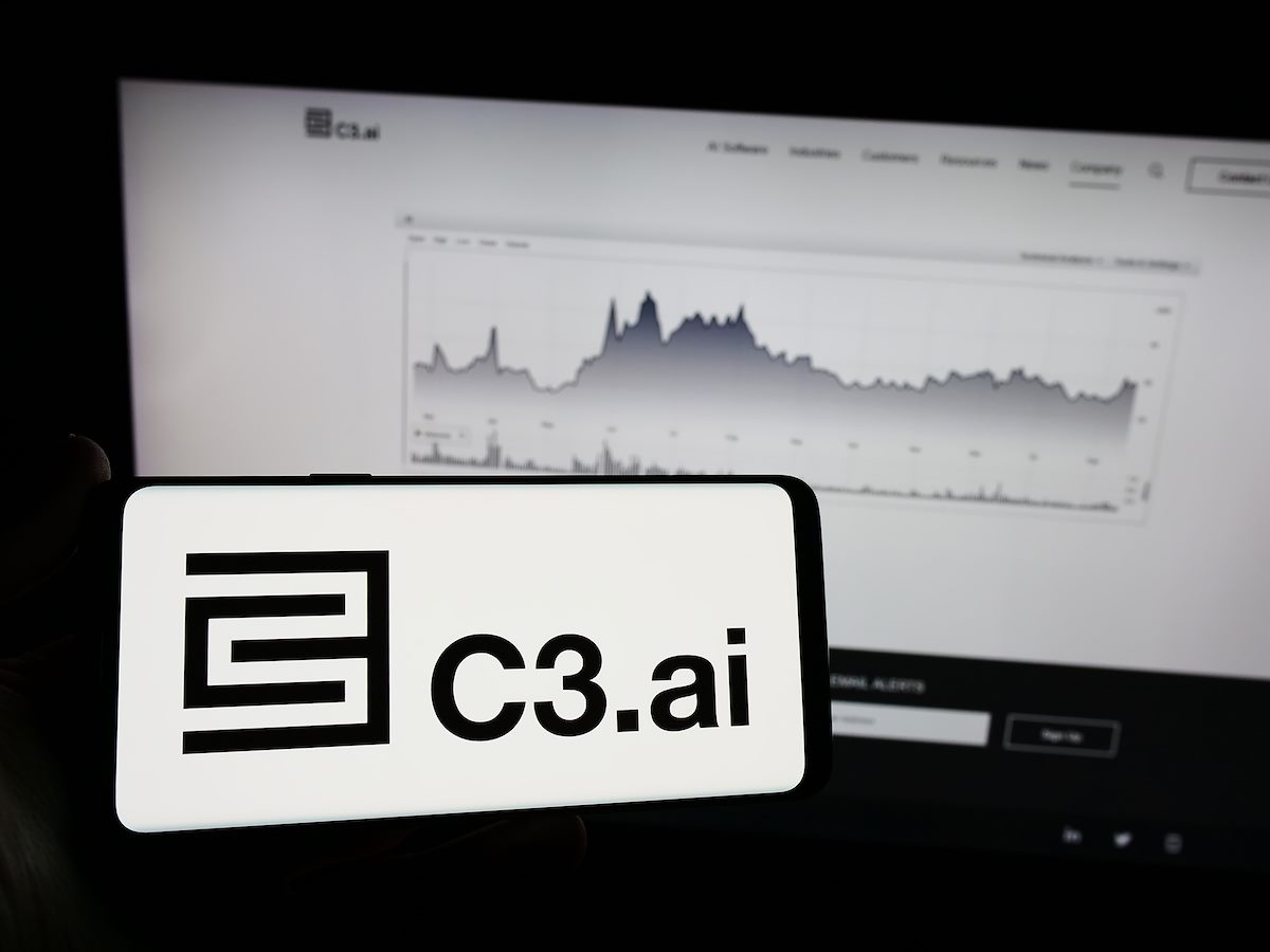 Person holding mobile phone with logo of American artificial intelligence company C3 AI in front of web page