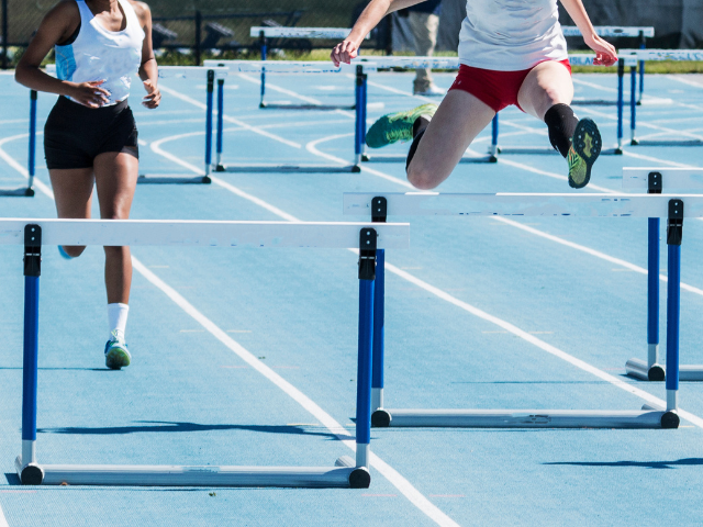 Two people on a track running a hurdle race. 