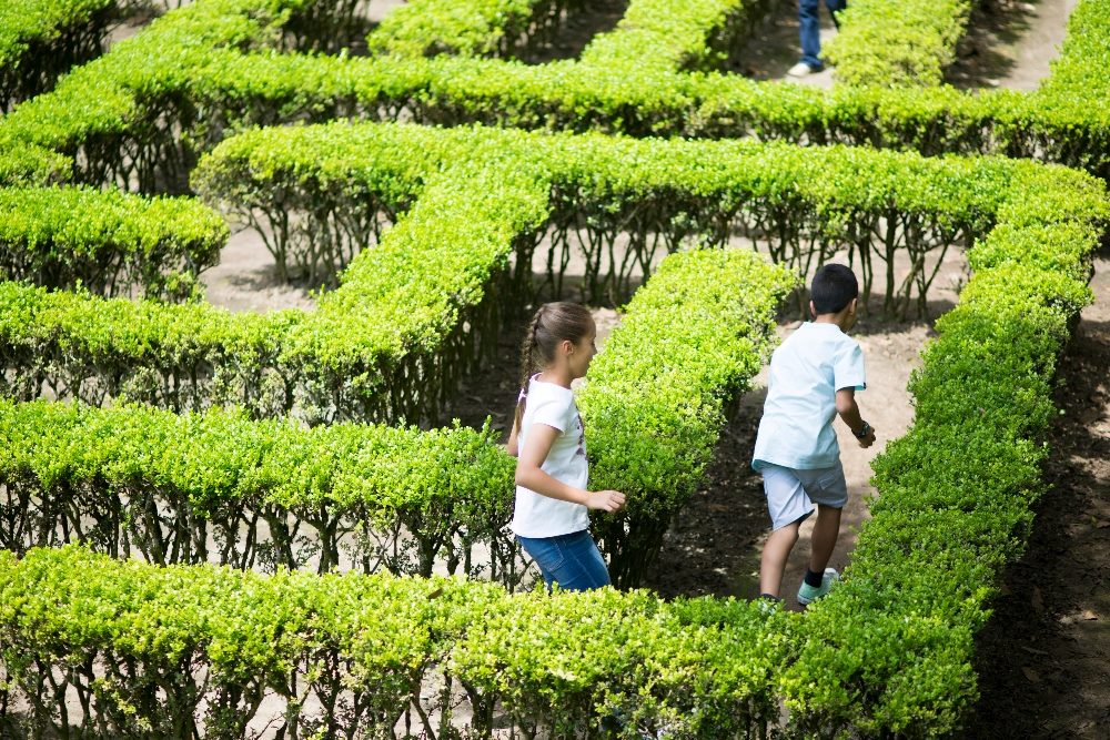 Two children navigate a maze of green hedges, symbolizing the challenges and complexities in AI customer service, emphasizing the need for effective strategies to guide users through automated interactions.