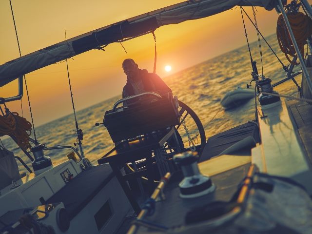  Sailor using wheel to steer rudder on a sailing boat.