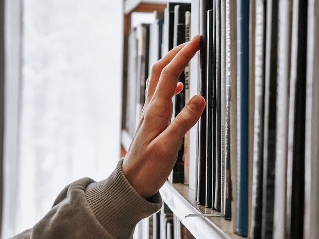 A hand running along a row of shelved books