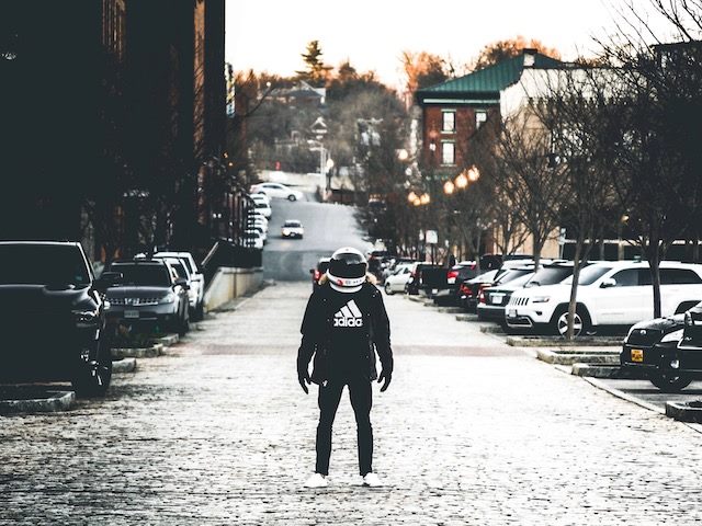 person standing in the middle of a city street wearing a motorcycle helmet looking like an astronaut