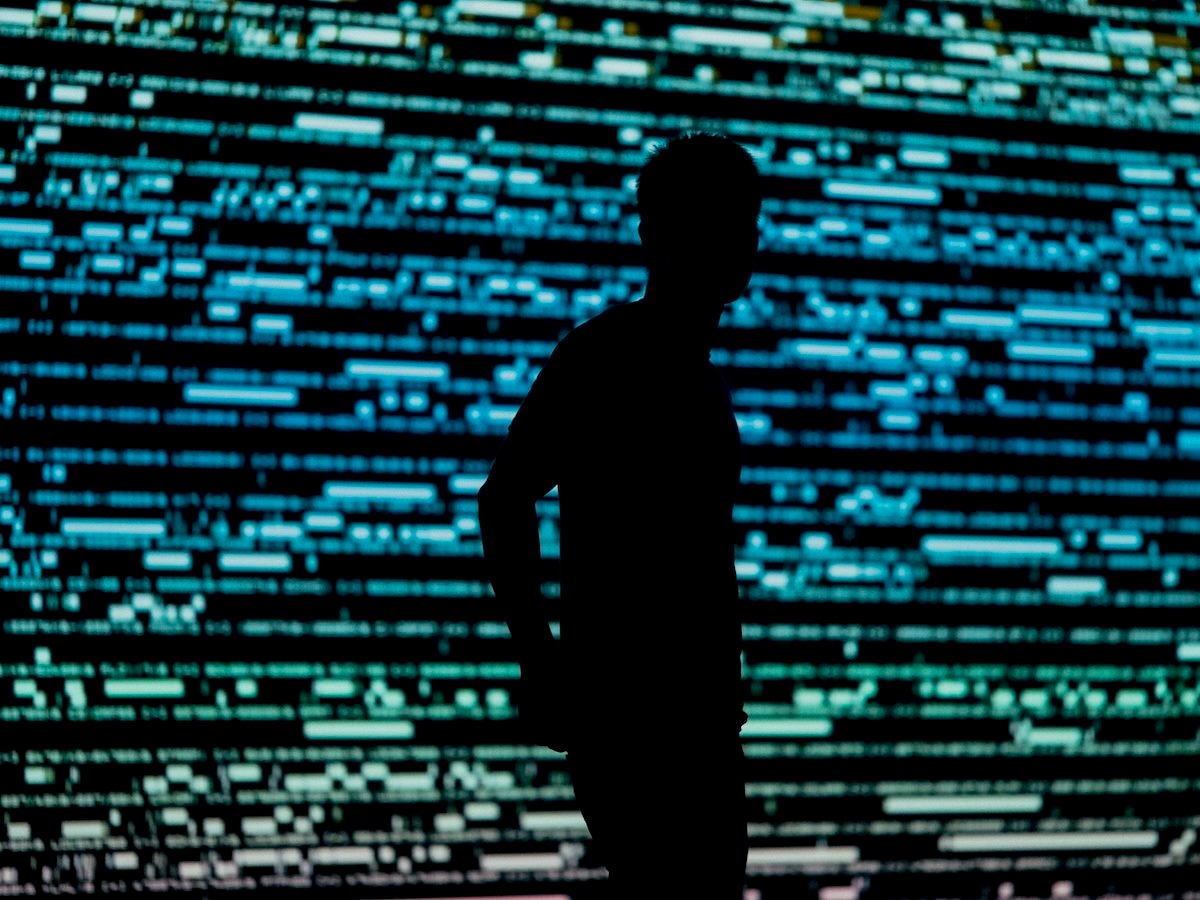 silhouette of a person standing against a digital wall with a display that looks similar to computer code