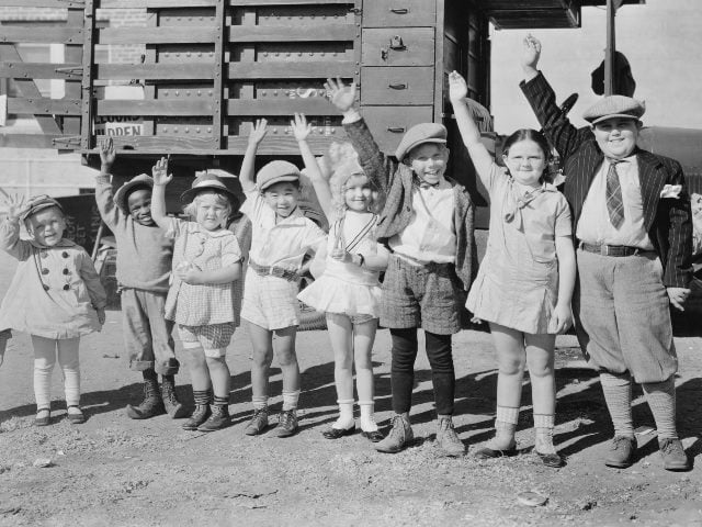A black-and-white photo with eight children lined up and waving.