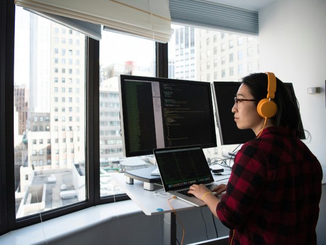 An employee works on a laptop with external monitors in a high-rise office.