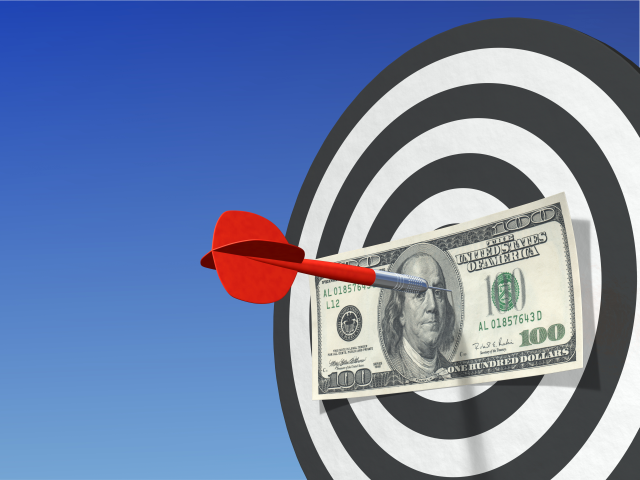 An outdoor archery target set against an azure colored sky. There is a $100 bill pinned to the target by a dart - right on the money concept