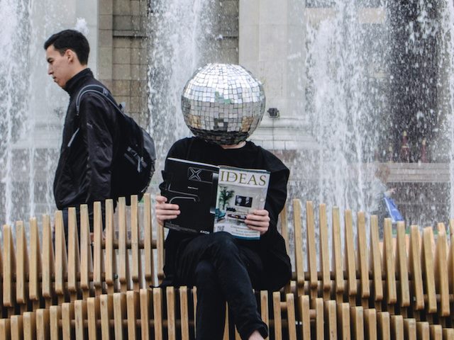 person with a disco ball where their head usually is, reading a magazine