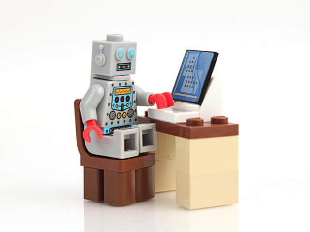 A Lego robot/AI working at a desk with a computer on it. Building chatbots concept