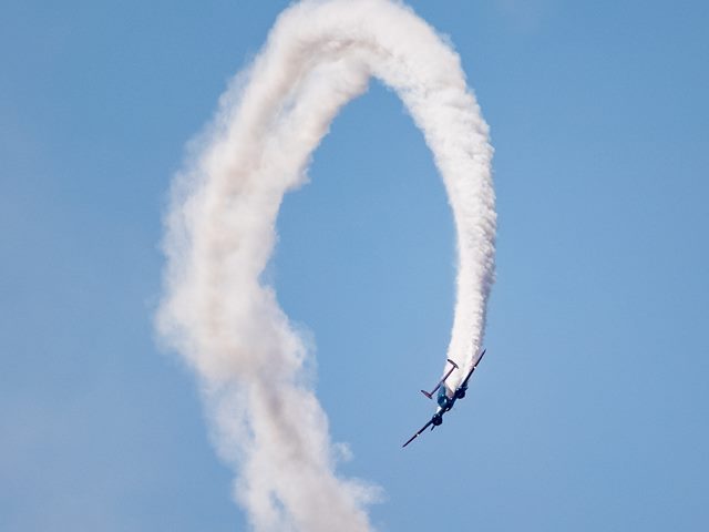 An airplane in flight leaving a trail of decorative smoke behind it as it does a loop trick.