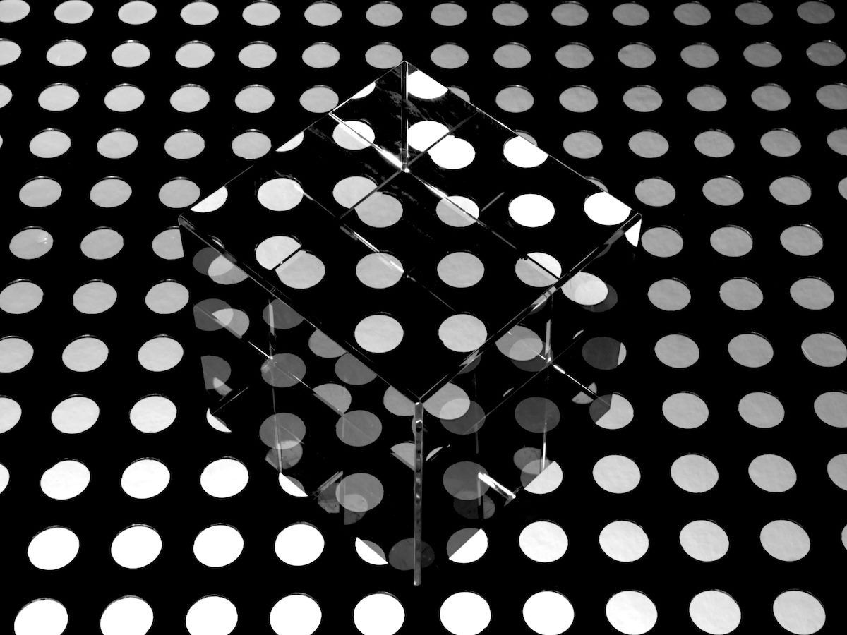 a clear cube disappearing against a polka dotted background