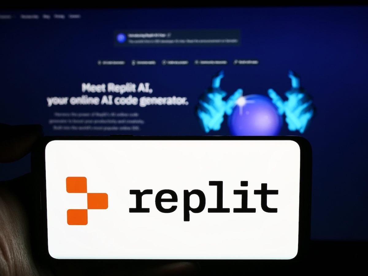 Person holding cellphone with logo of US software development platform company Replit Inc. in front of business webpage