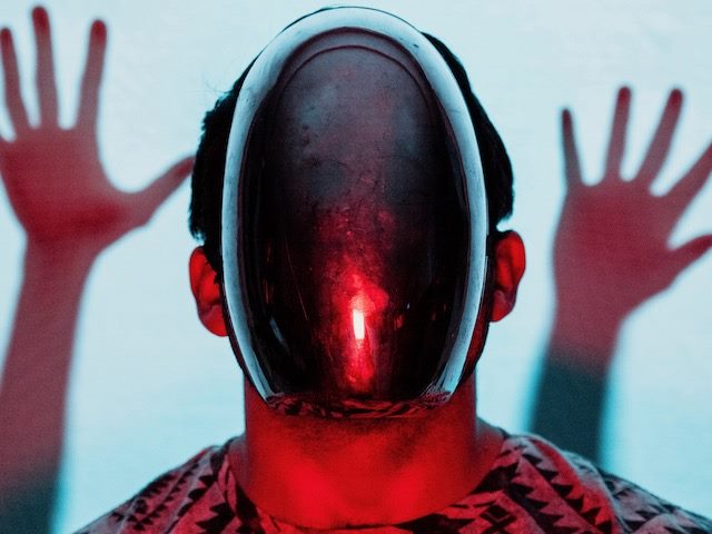 person with odd robot-like mask on - hands held up behind them