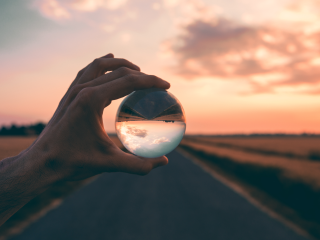 A man's hand holds a crystal ball peering through it to predict the future