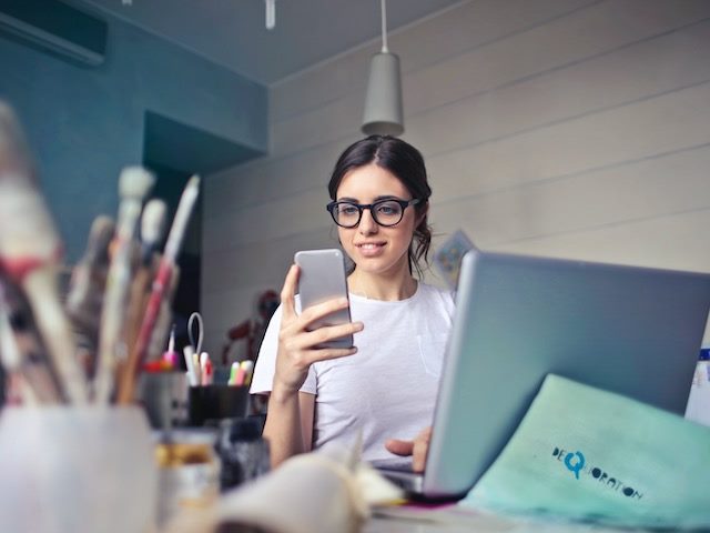 Young woman with smartphone near laptop