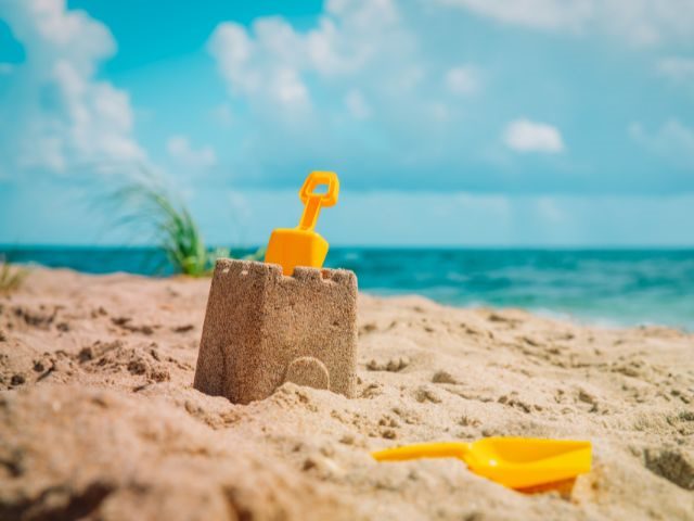 A sandcastle with two small shovels nearby and the beach behind 