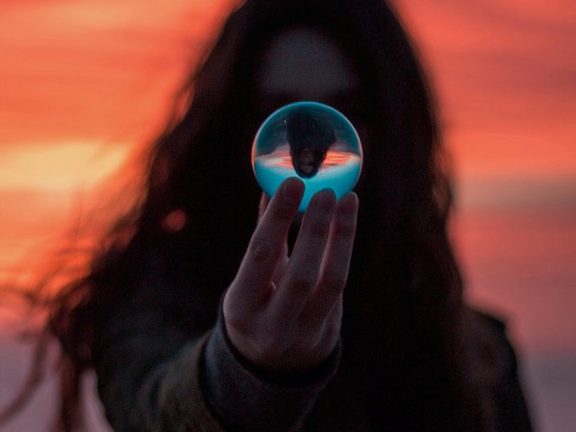 person holding  a glass ball with their image reflected upside down inside
