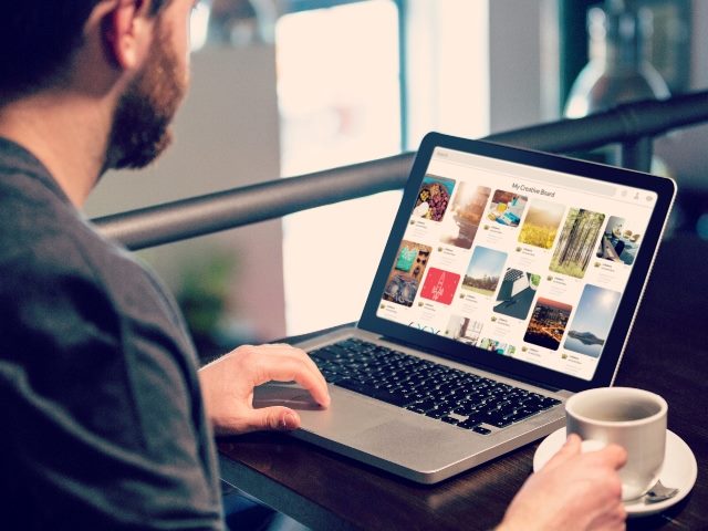 Man holding coffee mug while looking at a web page on his laptop. 