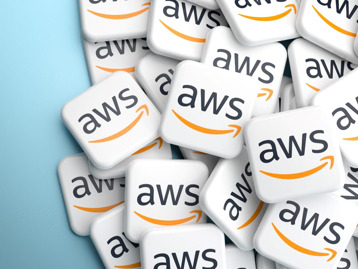 A pile of white square tiles with rounded corners, each displaying the AWS logo in dark gray text with the Amazon orange arrow smile graphic, stacked against a teal blue background.