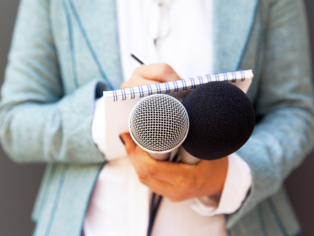 Female journalist at news conference, writing notes, holding microphone