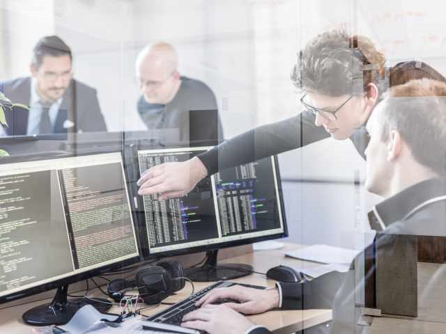 Young AI programmers and IT software developers team brainstorming and programming on desktop computer in the office.