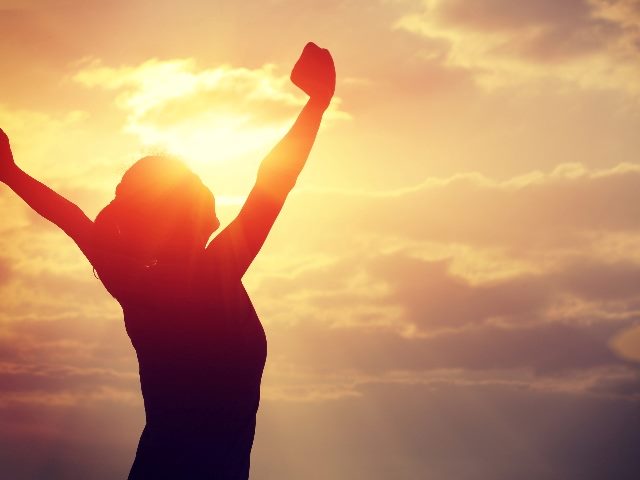A woman cheers and holds her arms up in the sky against a dramatic sunset suggesting he importance of AI in customer experience and metadat.
