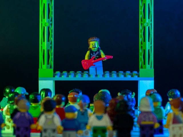 Lego rock star minifigure playing guitar and performing a solo concert on stage, just like AI customer experience tries to be a solo act for brands but can't win -- yet.