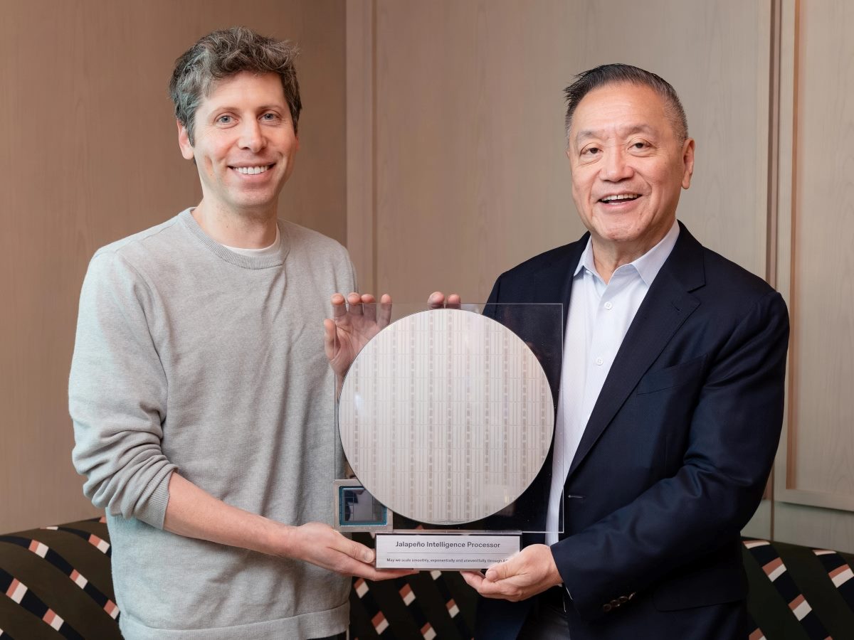 OpenAI CEO Sam Altman (left) and Broadcom President and CEO Hock Tan pose together holding a large silicon wafer and a packaged processor labeled "Jalapeño Intelligence Processor." Both are smiling as they display the AI chip hardware during a joint announcement.