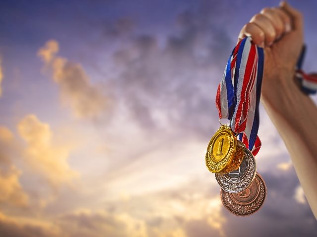 A hand shoots up into the air holding medals hanging from ribbons with a cloudy but golden sky in the background suggesting the need to champion agents.when introducing AI in  contact centers. 