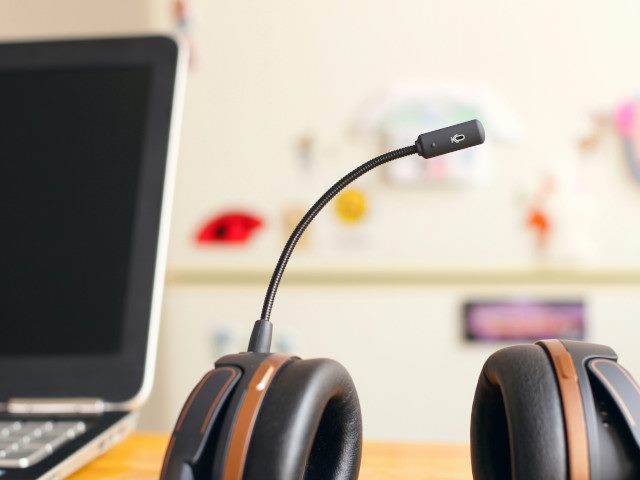 A headset on a desk next to a laptop computer.