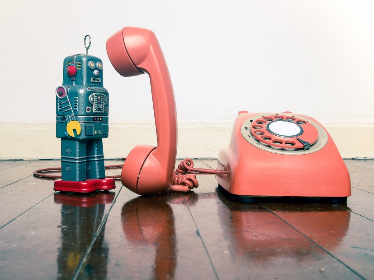 A grey robot standing next to a rotary phone