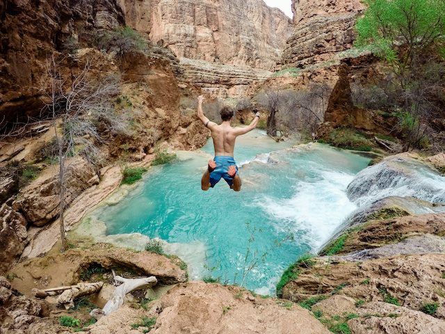 man in mid-air, jumping into a body of clear blue water