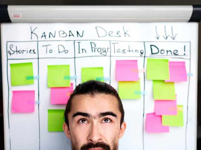 project manager with a kanban board desk behind him, implementing an agile marketing process.
