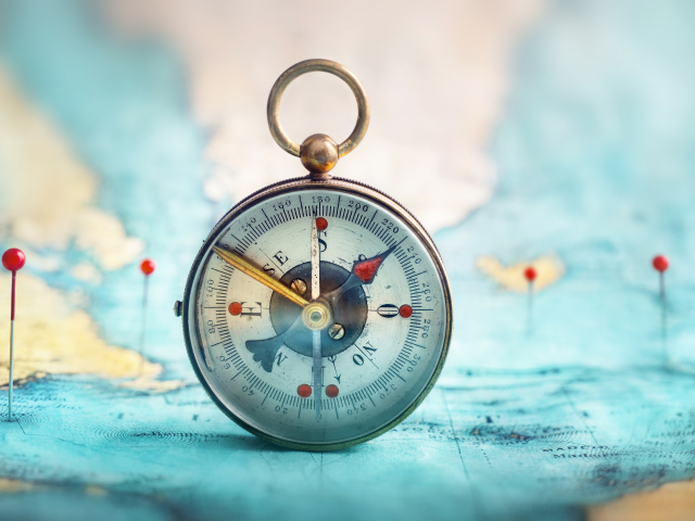 Magnetic compass and location marking with a pin on routes on world map. 