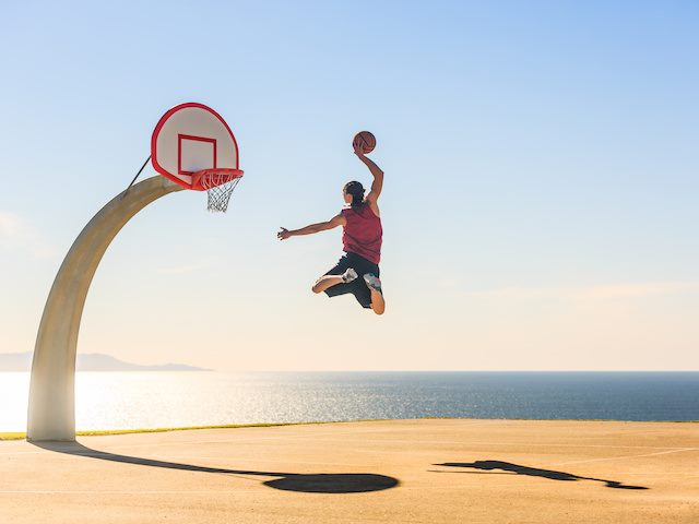 Basketball player jumping in the air on a court by the ocean